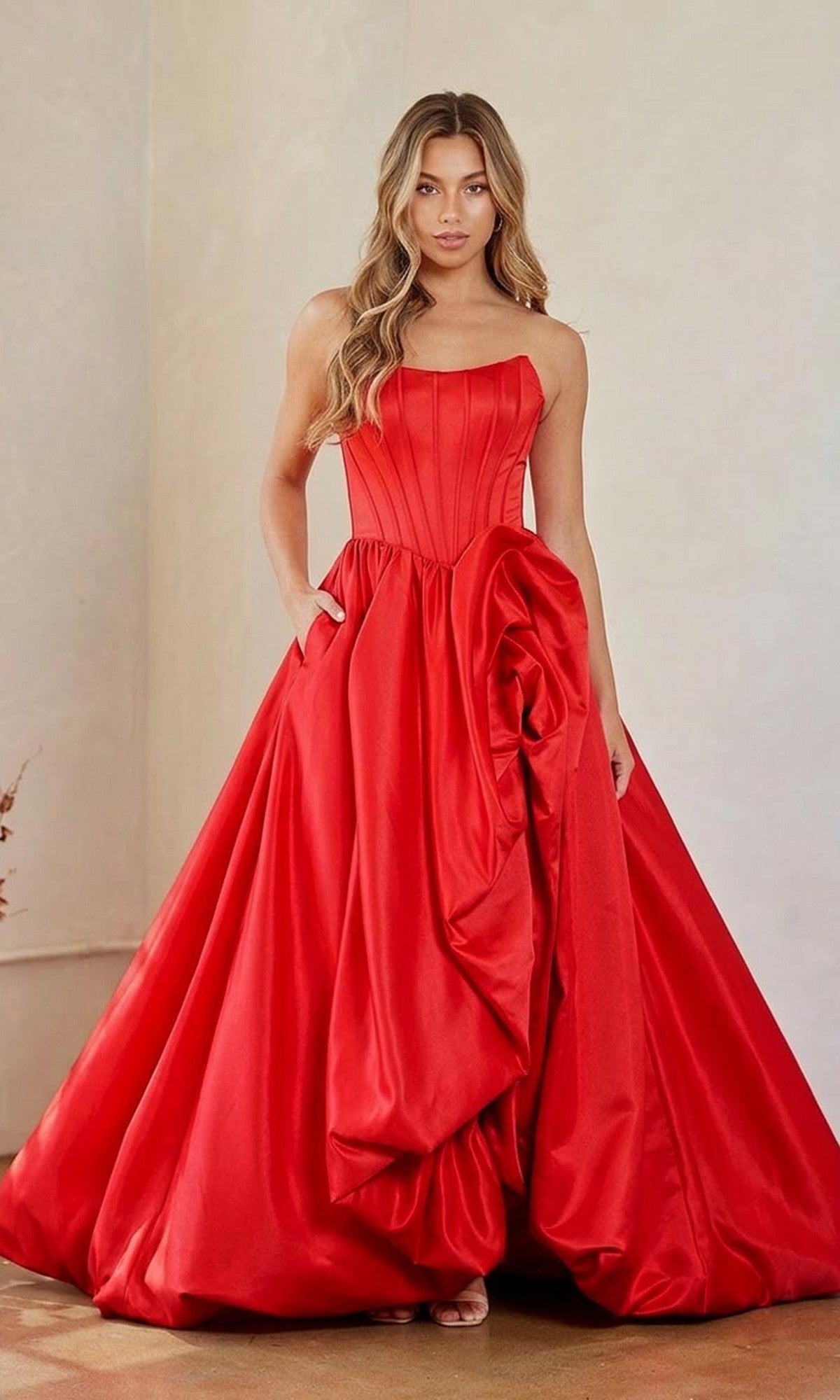 A woman wearing the Amelia Couture 2085 Long Prom Dress in red, featuring a strapless corset bodice and a voluminous skirt with dramatic gathered detailing.
